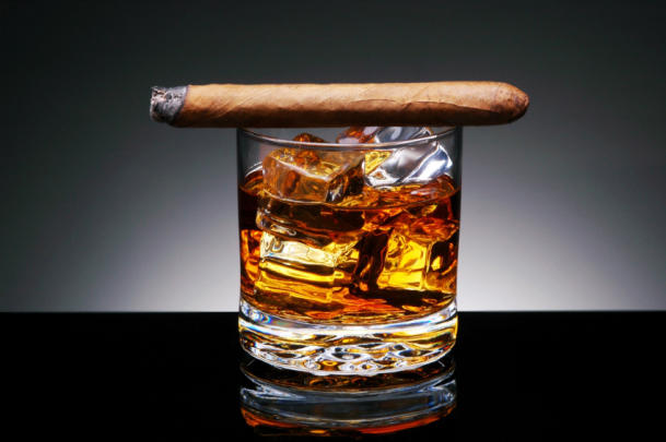Lit Cigar resting on Glass of Whiskey and Ice cubes
